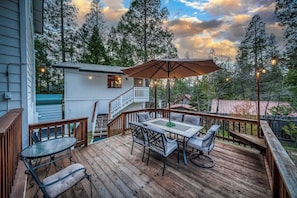 Eine Holzterrasse mit Tisch und Stühlen, ein kleines Gebäude mit Balkon und ein bewaldeter Hintergrund.