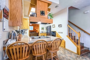 A kitchen with a central island, wooden chairs, a wooden staircase, and a view into the living area. - Black Bear Cabin - Boat Slip, Walk to Lake (Bass Lake)