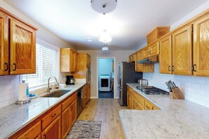 A kitchen with wooden cabinets, a granite countertop, a sink, and a stove. - Pine Place - Near Bass Lake & Yosemite (Oakhurst)