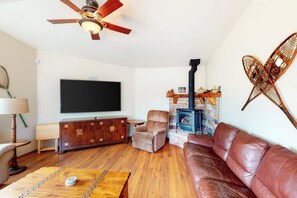 A living room with a television, a fireplace, a leather sofa, and a wooden coffee table. - Alder Lake View Lodge (Bass Lake)