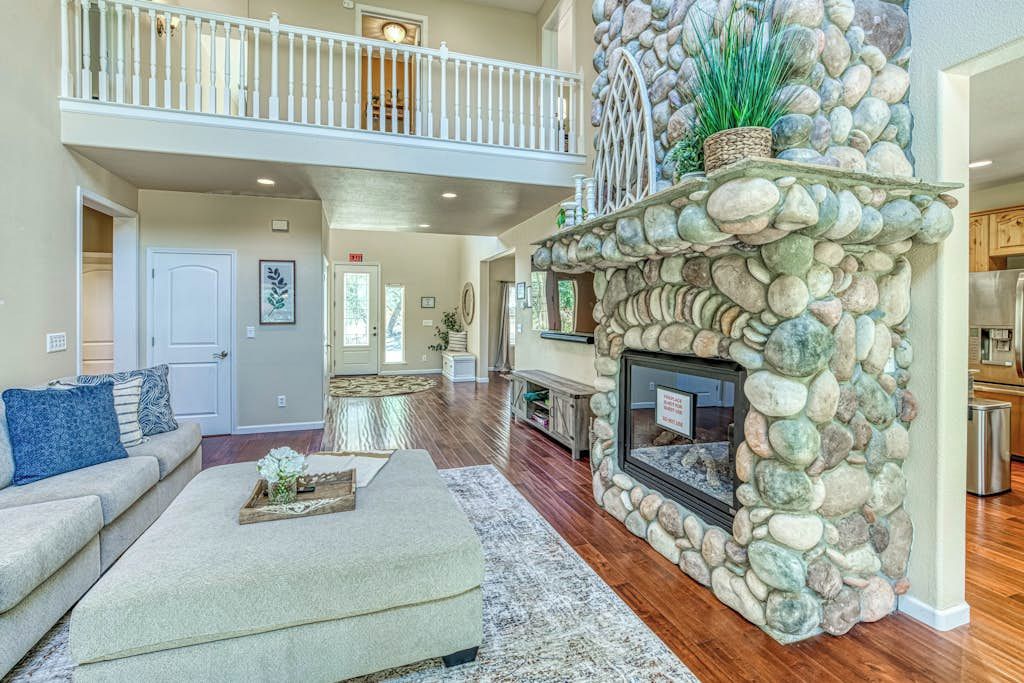 A spacious living area with a stone fireplace, a high ceiling, and a balcony.