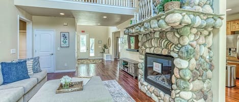 A spacious living area with a stone fireplace, a high ceiling, and a balcony.