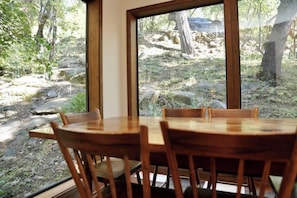 A dining area with a table and chairs, large windows offering a view of a rocky outdoor landscape. - Forest Glen - Secluded Cabin Inside Yosemite (Yosemite West)