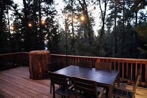 A wooden deck with a table and chairs, surrounded by trees and a wooden railing. - Forest Glen - Secluded Cabin Inside Yosemite (Yosemite West)