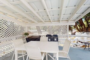 Une terrasse extérieure avec une table et des chaises blanches, un barbecue et une clôture en treillis blanche.
