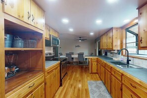Une cuisine avec des meubles de rangement en bois, une table à manger avec des chaises et un ventilateur de plafond.