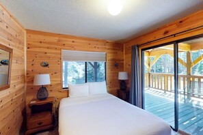 A wooden cabin bedroom with a bed, two bedside tables, and a large window. - Yosemite Big Rock Cabin (Fish Camp)