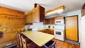 Eine kompakte Küche mit Holzschränken, einer zentralen Kochinsel mit Barhocker, einer Mikrowelle, einem Backofen und einem Kühlschrank.