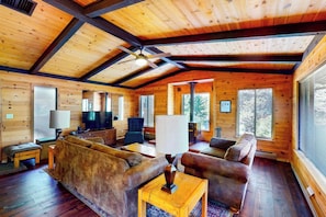 Ein Blockhaus-Interieur mit Holzbalkendecke, einer Sofagarnitur, einem Fernseher und einem Kamin.