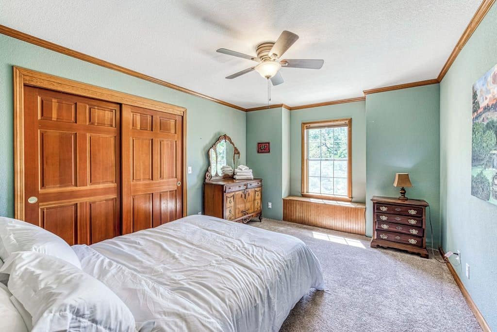 A bedroom with a bed, a dresser, a mirror, a window, and a ceiling fan.
