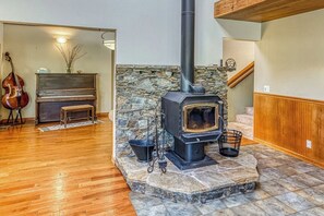 A room with a stone fireplace, a piano, and a cello stand. - Cascadel Haven - Mountain Views & Dog-Friendly (North Fork)
