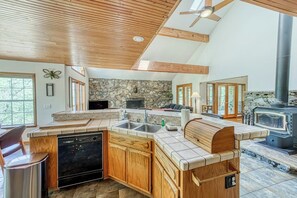 A spacious kitchen with a stone backsplash, wooden cabinetry, and a built-in dishwasher. - Cascadel Haven - Mountain Views & Dog-Friendly (North Fork)