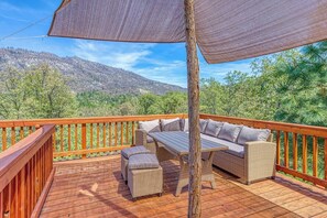 A wooden deck with outdoor furniture, including a sofa and a table, overlooking a mountainous landscape. - Cascadel Haven - Mountain Views & Dog-Friendly (North Fork)