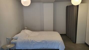 Een slaapkamer met een bed, nachtkastje, lamp en gordijnen.