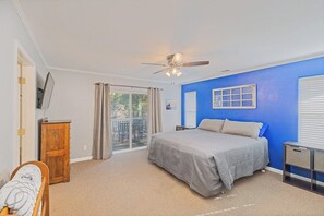 Une chambre à coucher comprenant un lit, un ventilateur de plafond, une armoire en bois, un bureau et une vue sur l’extérieur grâce à une porte-fenêtre coulissante.