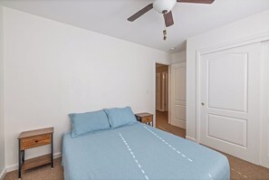 Ein Schlafzimmer mit einem Bett, einem Nachttisch, einem Deckenventilator und einer Tür.