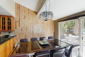 A modern dining area with a glass table, leather chairs, and a wooden wall. - Todds Lakefront House (Bass Lake)