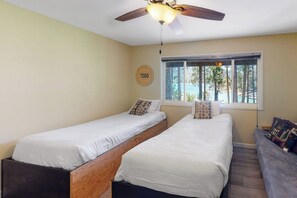 A bedroom with two single beds, a ceiling fan, a window with a view, and a round wall decoration. - Todds Lakefront House (Bass Lake)