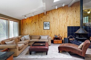 Ein Wohnzimmer mit einer Holzwand, einer Sofagarnitur, einem Ledersitzhocker, einem Kamin und einem gerahmten Bild an der Wand.