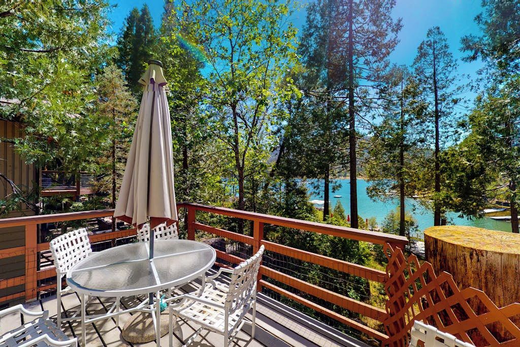 A balcony with a table and chairs, overlooking a forest and a body of water.