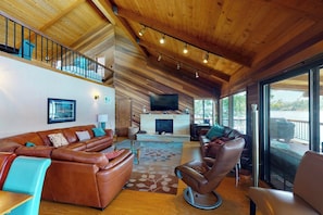 A spacious living area with a wooden ceiling, a fireplace, leather sofas, and a large window offering a view of the outdoors. - Peters Lakefront - Dock, Pool Table & Lake Views (Bass Lake)