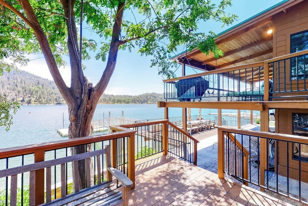A wooden deck with a view of a lake, a tree, and a building with a balcony.