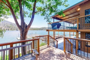 Una terraza de madera con vista a un lago, un árbol y un edificio con balcón.