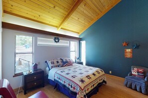Un dormitorio con techo de madera, una cama con colcha, una mesita de noche, una silla y una pared decorada con estrellas.