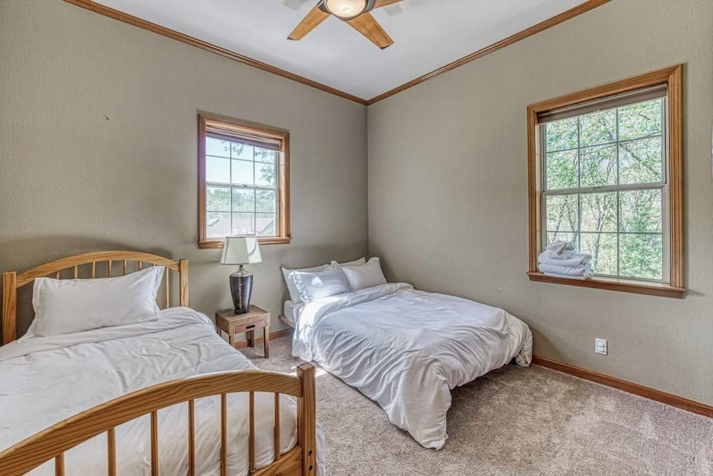 A bedroom with two beds, a ceiling fan, a window, and a nightstand.