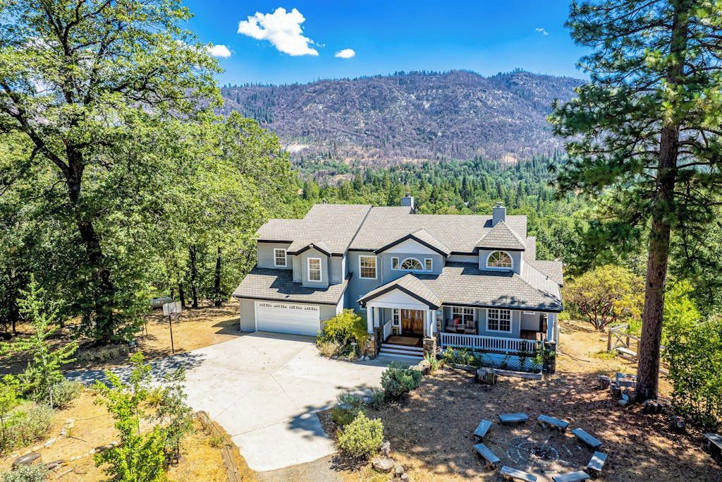 A two-story house with a front porch, garage, and a view of a forested mountain range.