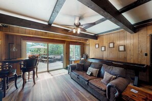 Ein Zimmer mit Holzboden, Deckenventilator, einer Couch, einem Esstisch und Stühlen.