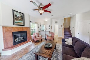 A living room with a fireplace, a ceiling fan, and a staircase leading to another level. - Willard Lake House - Heated Pool, Hot Tub & Views (Bass Lake)