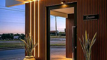 Entrada de un hotel con una recepción, dos plantas grandes en macetas y vista a la calle.