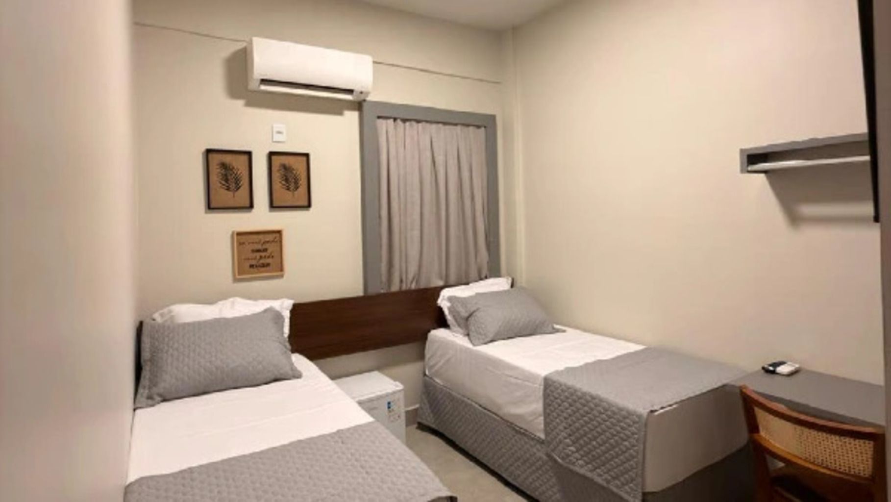 Quarto de hotel com duas camas de solteiro, uma escrivaninha e uma cadeira.
