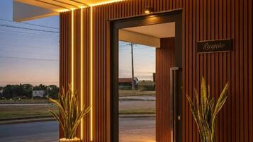 A reception area with a wooden facade and a sign that reads 'Recepção.' There are two potted plants in front of the entrance.