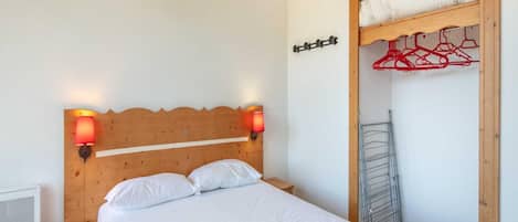 A single bed with a wooden headboard, two wall-mounted lamps, a small bedside table, and a built-in wardrobe with a drying rack.