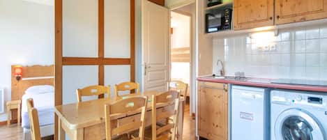 Une cuisine compacte dotée de meubles en bois, d’un four à micro-ondes, d’un lave-linge et d’un coin repas avec une table et des chaises.