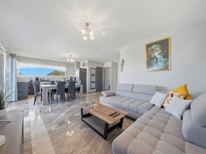 A modern living room with a sofa, a coffee table, and a dining area with chairs and a table. - Le Solévin · Vue vignes & Pic Saint-Loup - 4p (Jacou)