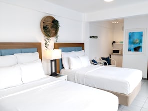 A hotel room with two beds, a bedside table, a lamp, a microwave, and a small seating area. - Suite 7 at Trinitaria House Hotel (San Juan)