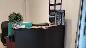 Un mostrador de recepción con un monitor de computadora, una planta en maceta y un certificado enmarcado.