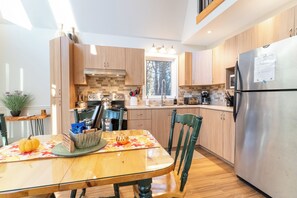 A modern kitchen with wooden cabinets, a stainless steel refrigerator, and a dining table with chairs.