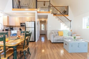 A spacious living area with a staircase, a kitchen with modern appliances, and a dining table set.