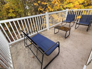 A covered outdoor seating area with a white railing, two blue lounge chairs, and a small table.