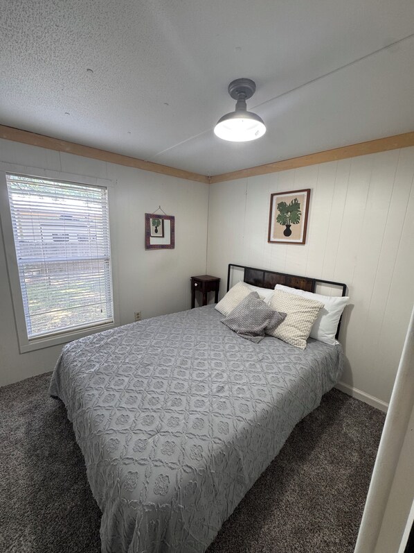 A bedroom with a bed, a ceiling fan, a window with blinds, and two framed pictures on the wall.