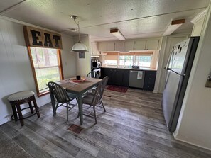 A kitchen with a dining table, chairs, a refrigerator, and a window with blinds.