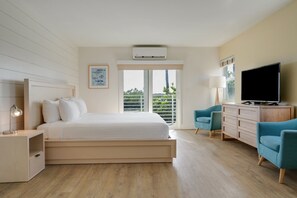Ein modernes Hotelzimmer mit einem großen Bett, einem Fernseher, einem Schreibtisch mit Lampe und Blick ins Freie durch das Fenster.
