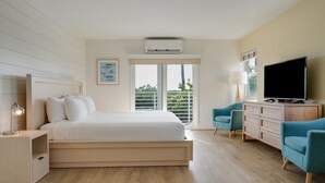 Moderni hotellihuone, jossa on suuri sänky, televisio, työpöytä lampun kanssa ja ikkunasta avautuva näkymä ulos.