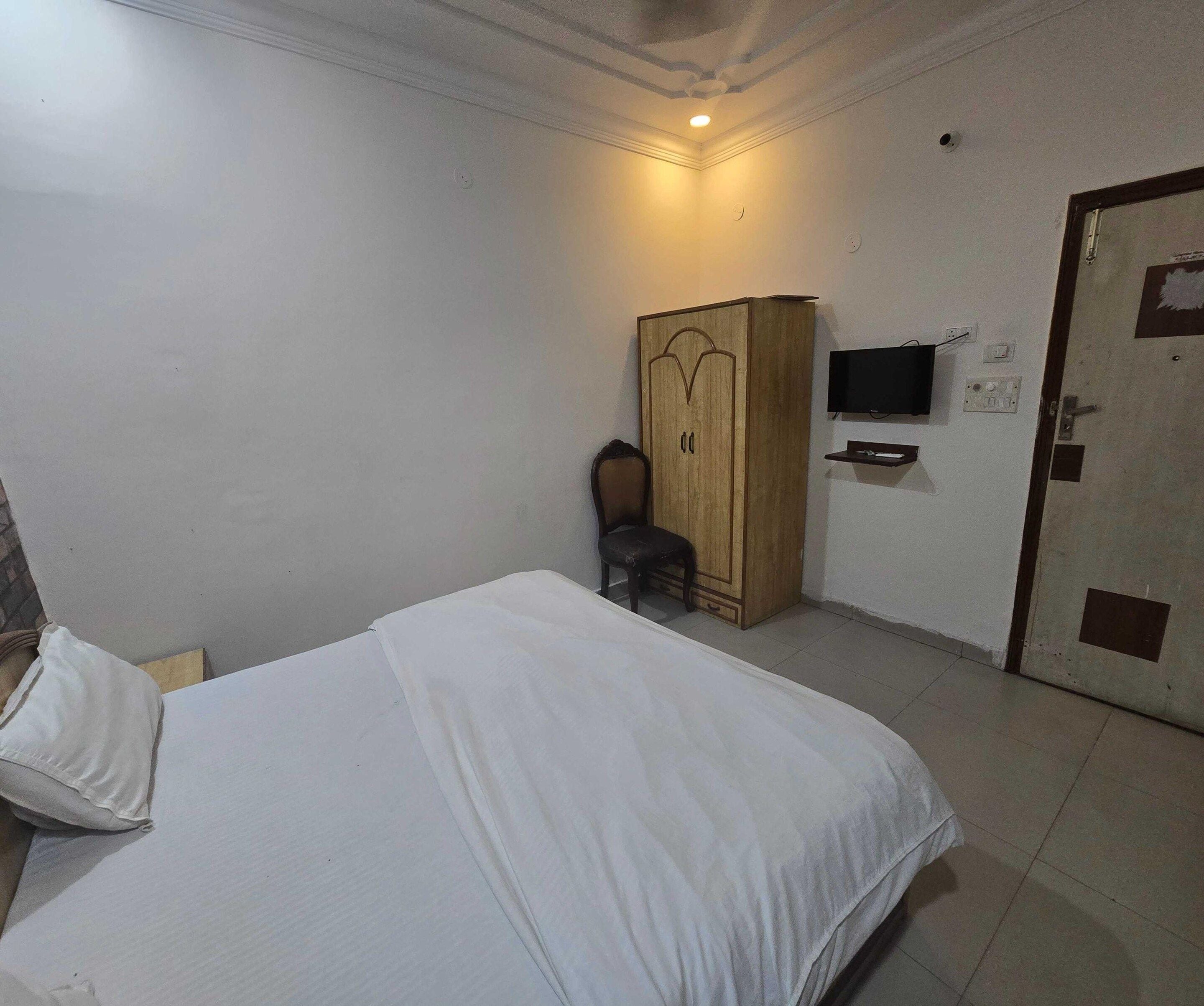 A bedroom with a bed, a wardrobe, a chair, a television, and a door.