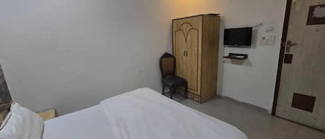 A bedroom with a bed, a wardrobe, a chair, a television, and a door.