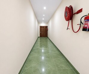 A hallway with green marble flooring, a wooden door at the end, and a red fire hose mounted on the wall. - Deluxe Room Hotel Tashi (Amritsar)
